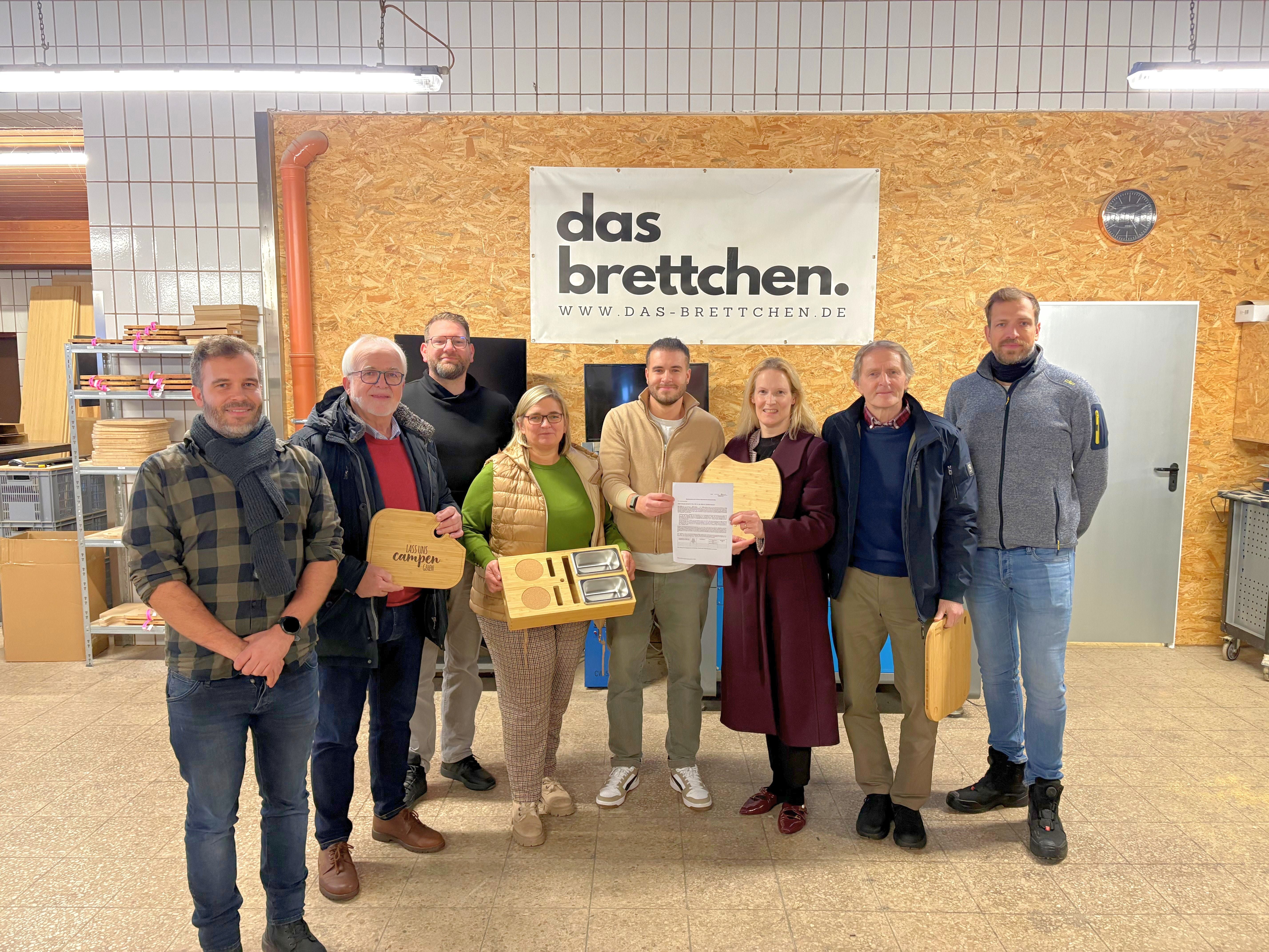 Personen mit Produkten in Werkstatt bei der Übergabe eines Förderbescheids