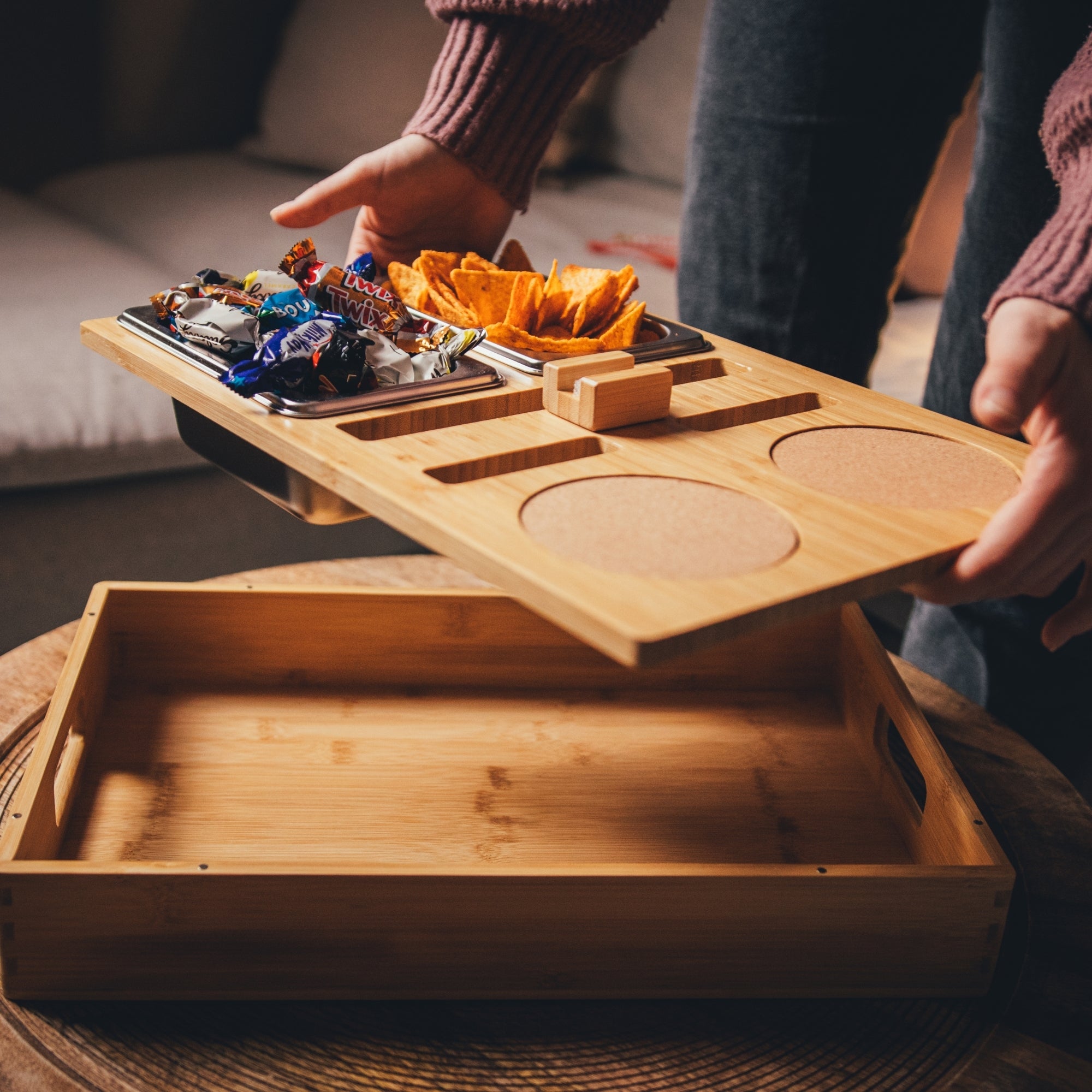 Personalisierbare Couchbar aus Holz mit integrierten Getränkehaltern, Snackfächern und Kork-Untersetzern, gefüllt mit Chips und Süßigkeiten, ideal für gemütliche Fernsehabende auf dem Sofa