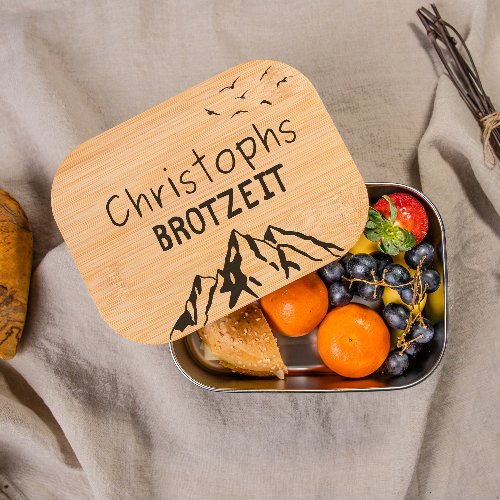 Personalisierte Edelstahl-Lunchbox mit Bambusdeckel, graviert mit 'Christophs Brotzeit' und Bergmotiv, gefüllt mit Obst und Brötchen, ideal für Schule, Arbeit oder Picknick
