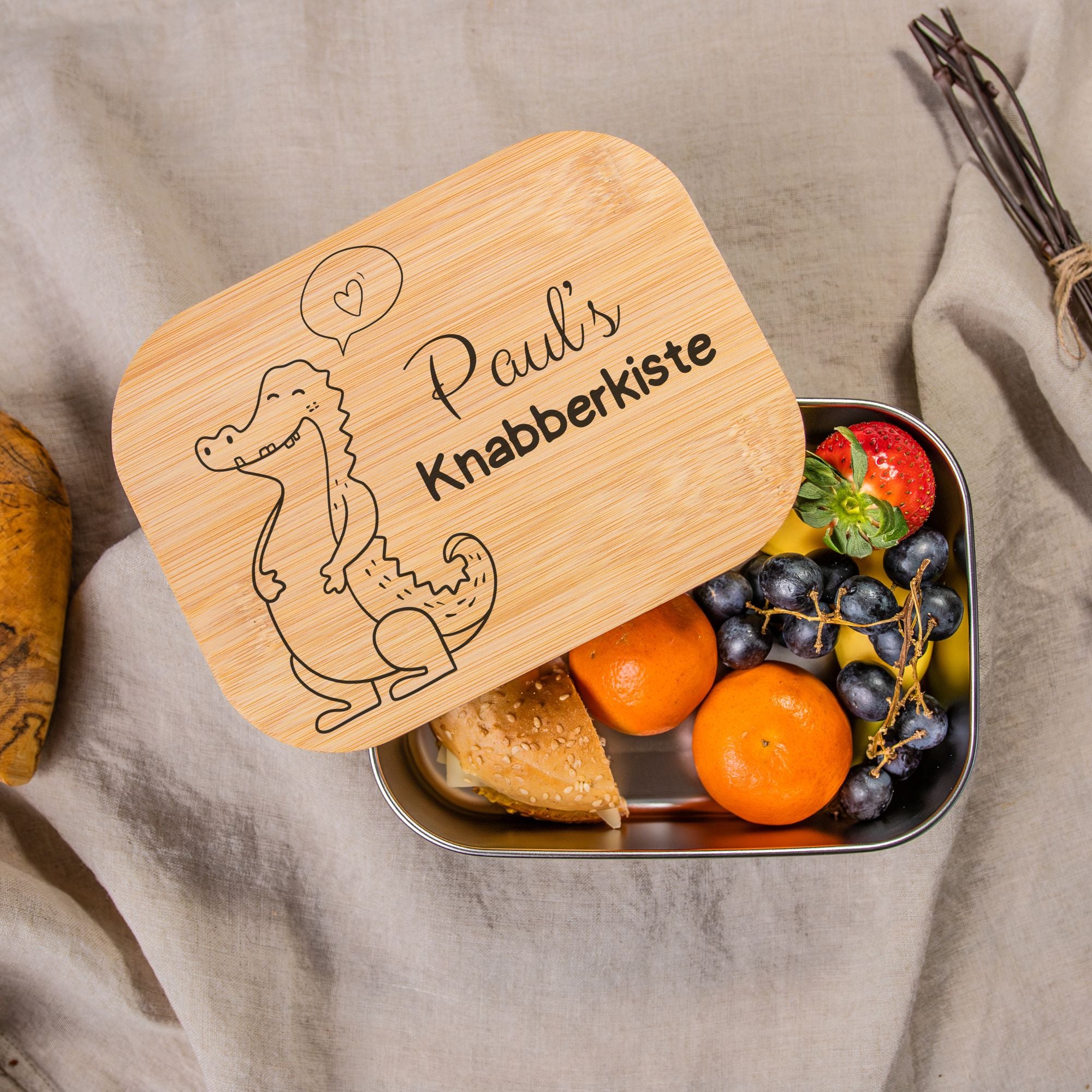 Personalisierte Edelstahl-Lunchbox mit Bambusdeckel, graviert mit 'Paul's Knabberkiste' und Krokodil-Motiv, gefüllt mit Obst und Brötchen, ideal für Kinder in Schule und Kindergarten